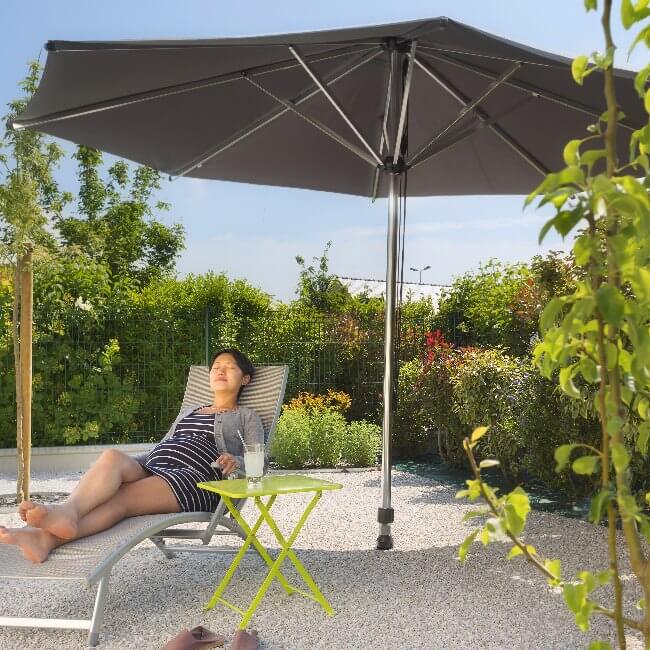 Femme se relaxant dans son jardin au soleil sous un parasol droit