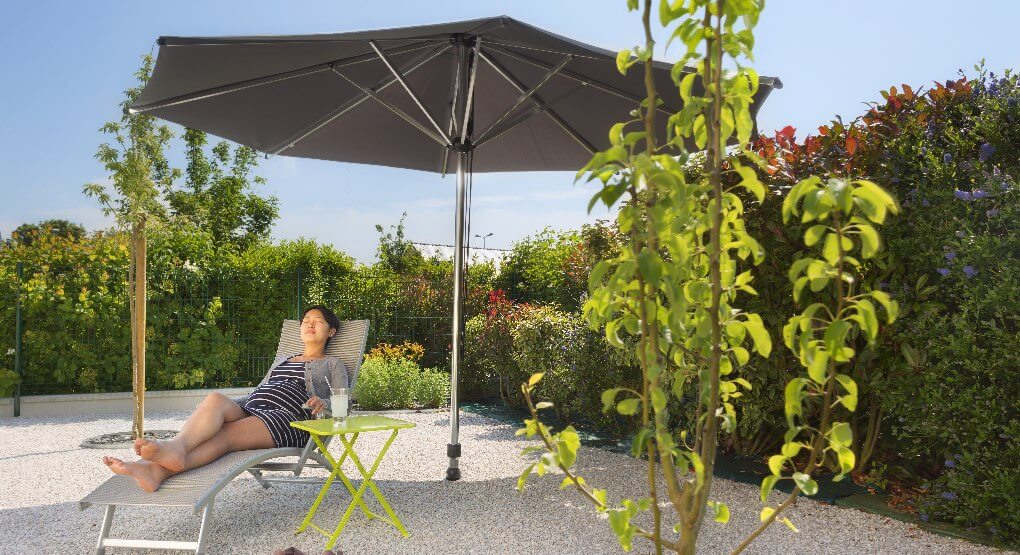 Femme se relaxant dans son jardin au soleil sous un parasol droit