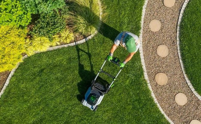 Un jardinier tond une pelouse avec une tondeuse thermique